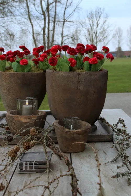Donkerroze kunstbloemen madeliefjes in houten potten op buitentafel met kaarsen en natuurlijke decoratie