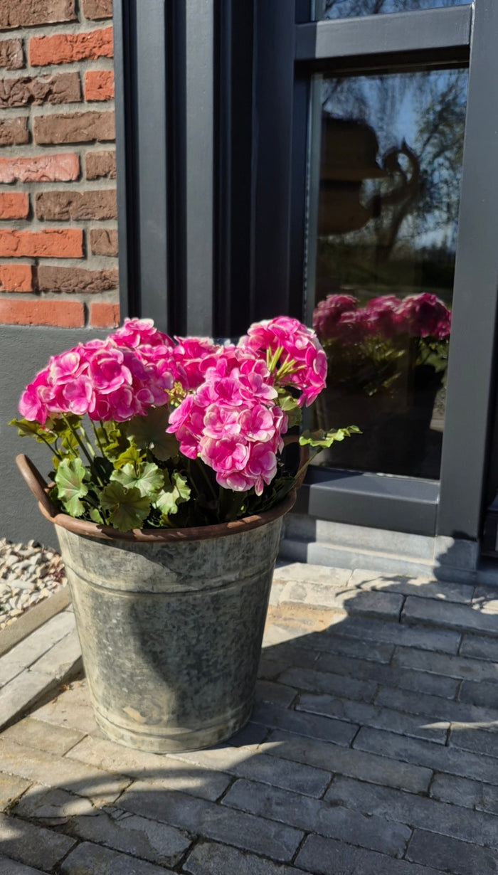 Roze geranium buiten kunstplant in zinken emmer